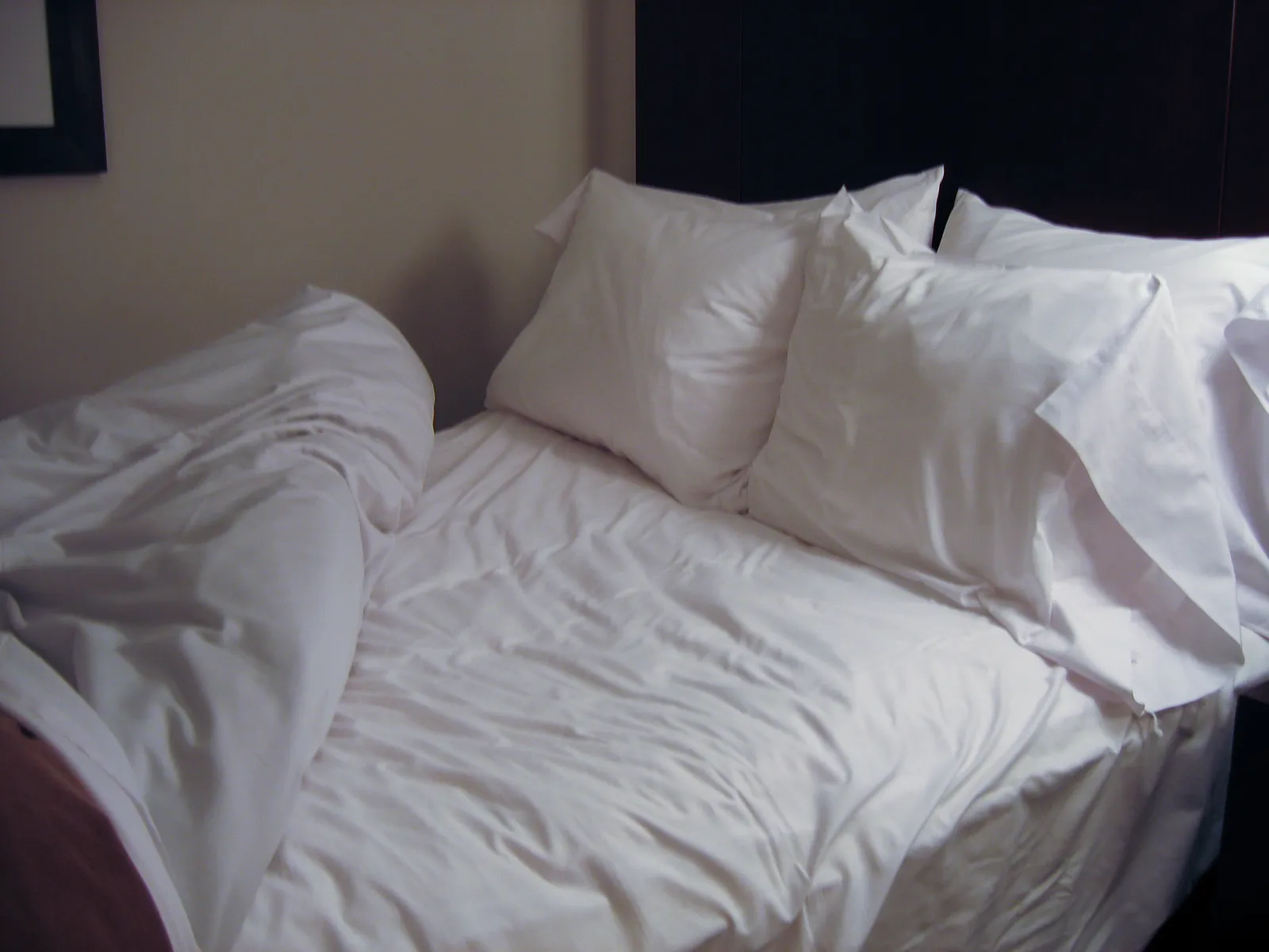 Lit défait aux draps blancs froissés, avec quatre oreillers moelleux contre une tête de lit sombre