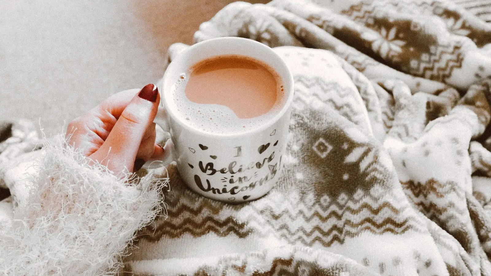 Mains tenant une tasse chaude sous un plaid douillet, ambiance cocooning d'hiver