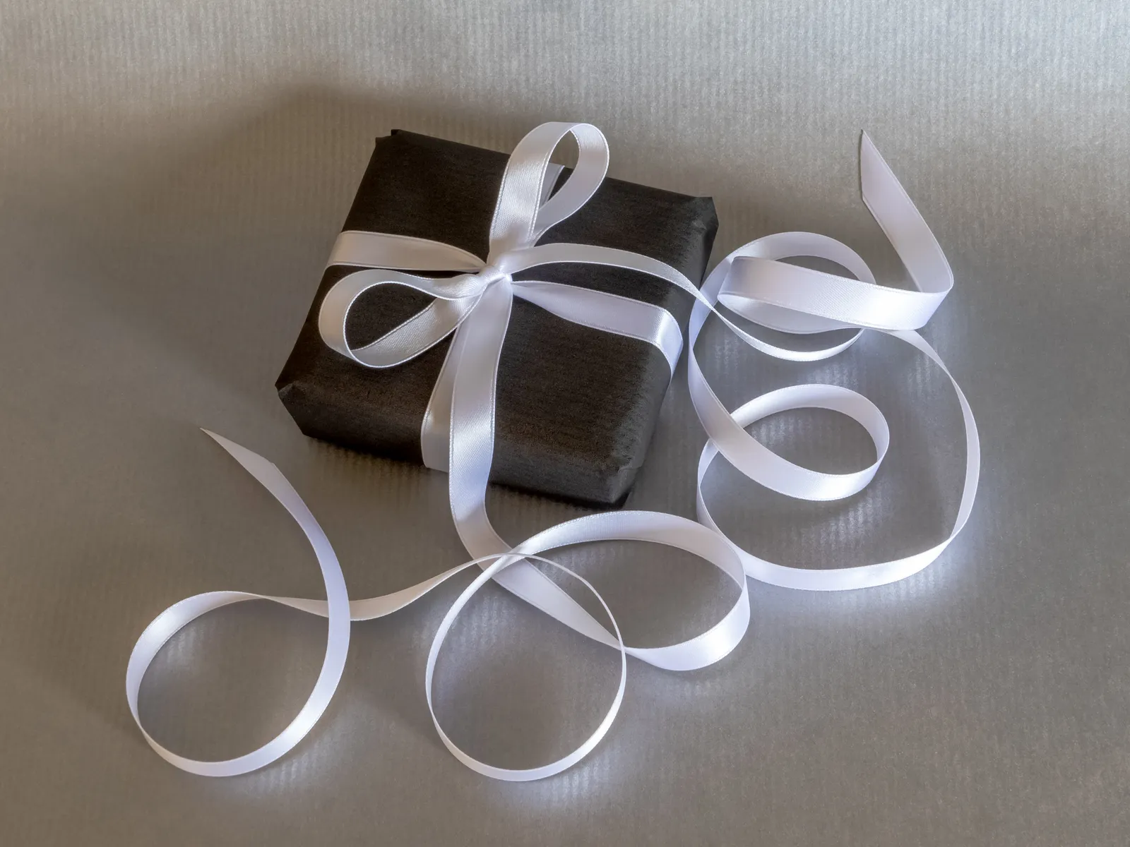 Paquet cadeau emballé de papier noir et noué d'un long ruban de satin blanc