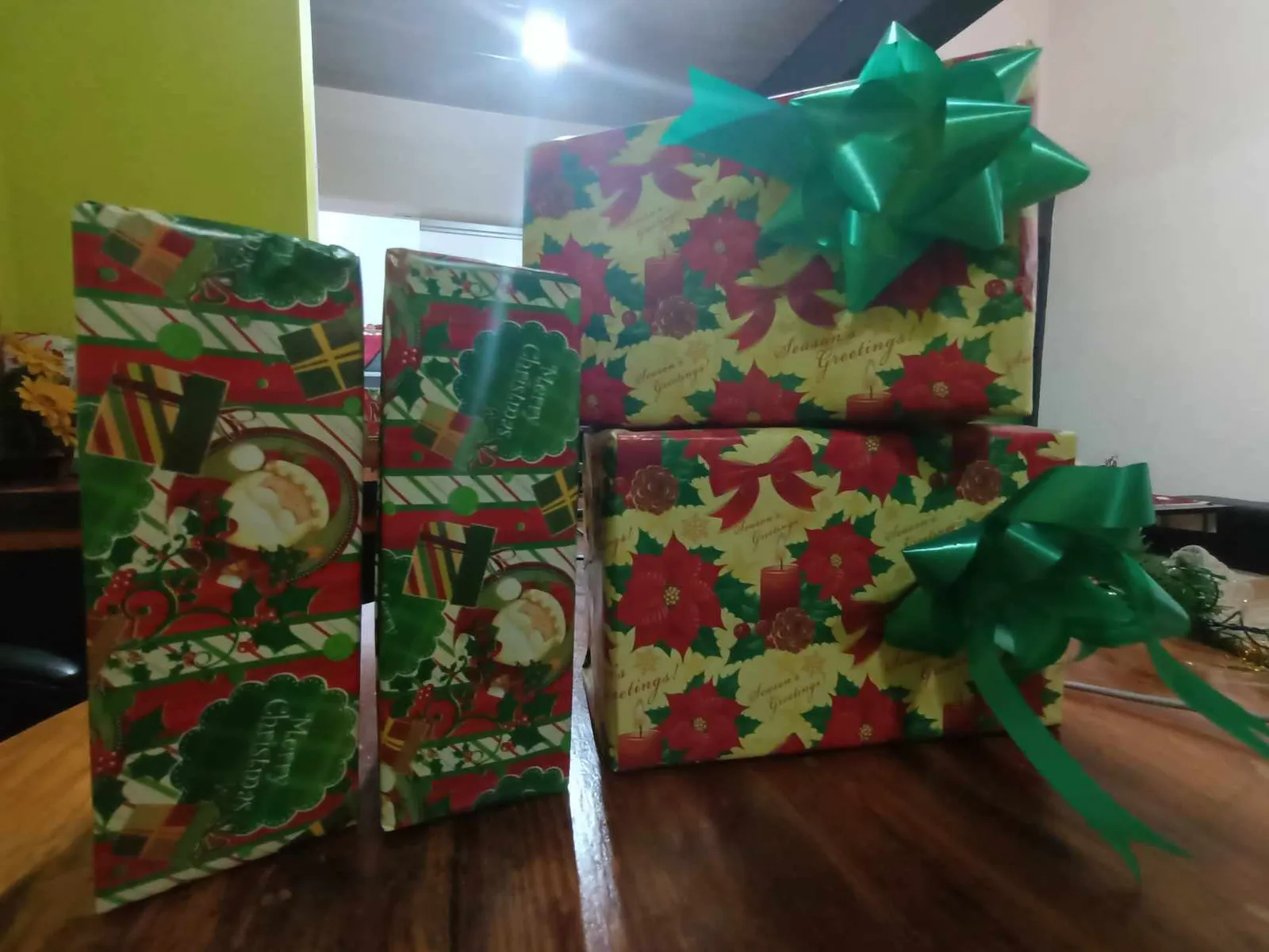 Trois paquets cadeaux emballés de papier de Noël à motifs, ornés de nœuds verts, posés sur une table en bois